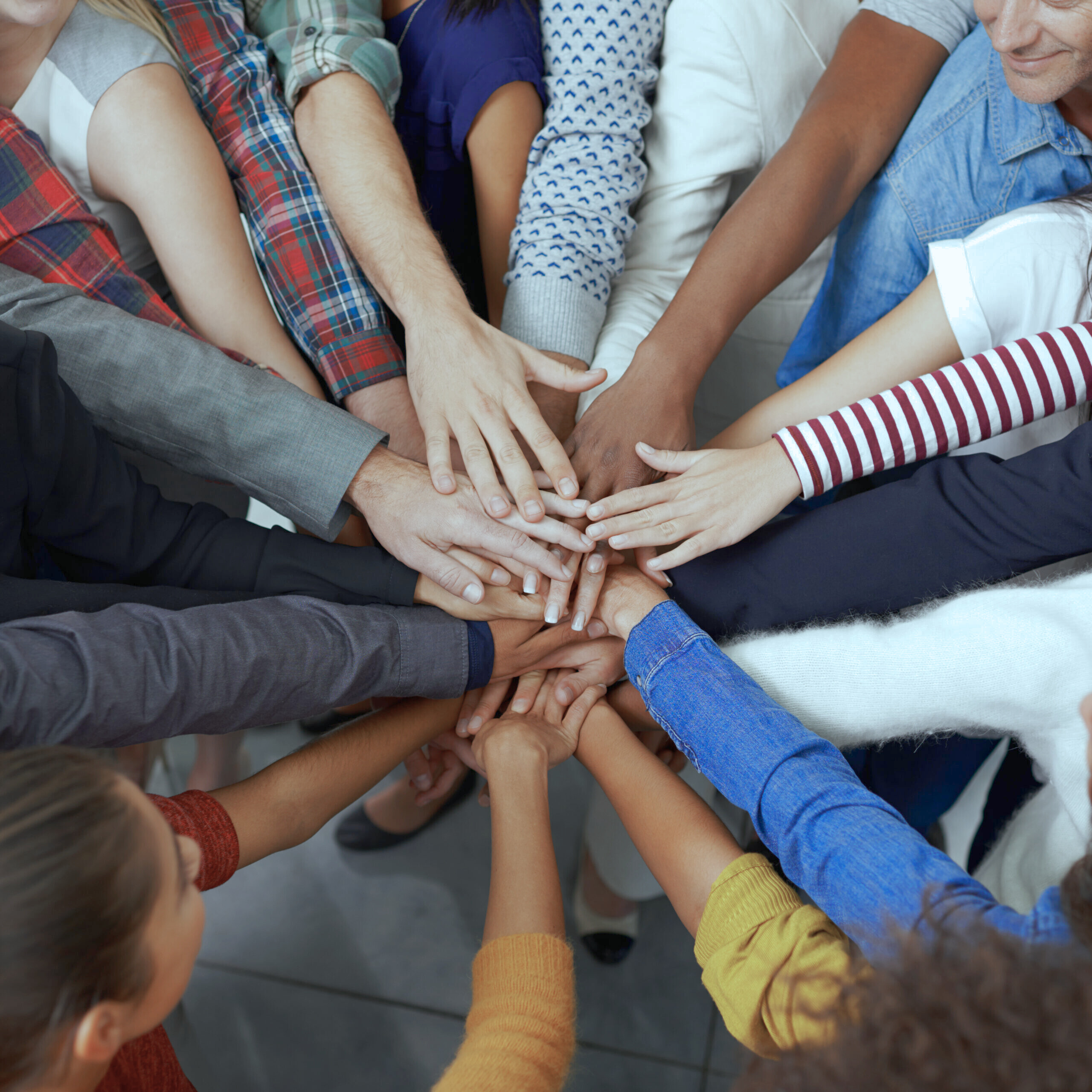 Mehrere Menschen legen ihre Hände übereinander – Symbol für Teamarbeit, Zusammenhalt und Integration.